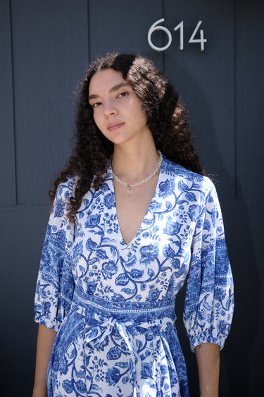 A woman wearing a blue and white floral caftan with three quarter balloon sleeves and an obi belt.