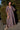 A woman wearing a maxi caftan with a floral pattern in a color that could be described as blue ground with tan, brown and coral, standing outdoors.