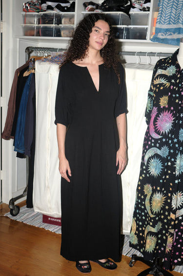 A woman standing inside wearing a black maxi dress with shape from princess panels.