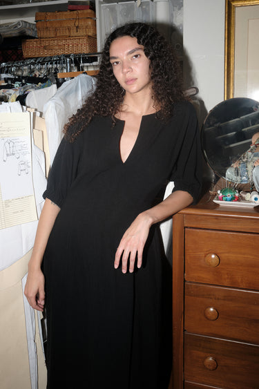 A woman standing inside wearing a black maxi dress with shape from princess panels.