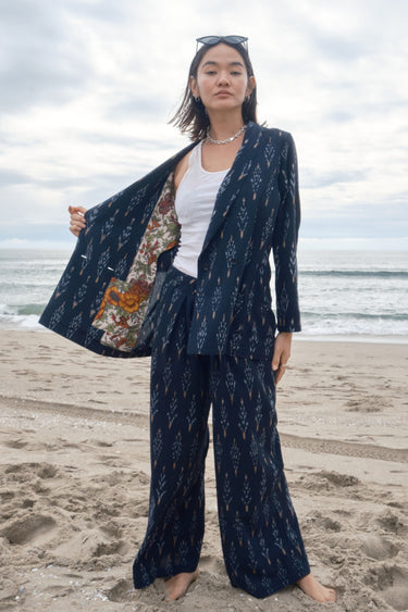 Woman at the beach wearing an ikat double breasted jacket with matching trousers, showing the half lining and pocket.