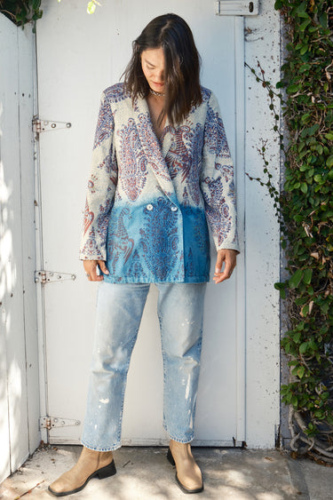 A woman wearing a double-breasted jacket with an indigo and blue pattern jacket, over jeans. The jacket is dipped in indigo dye and has pockets on the inside.
