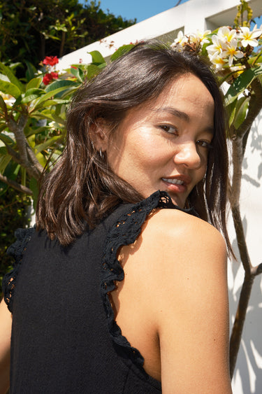 Woman wearing a black sleeveless dress - caftan standing outdoors against a white wall.