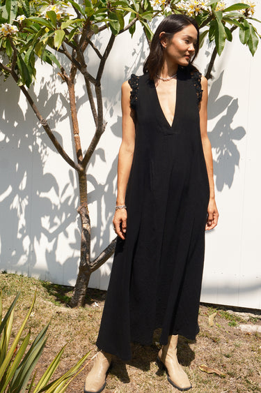 Woman wearing a black sleeveless dress - caftan standing outdoors against a white wall.
