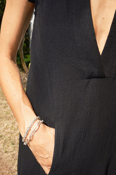 Woman wearing a black sleeveless dress - caftan standing outdoors against a white wall. Detail of pocket