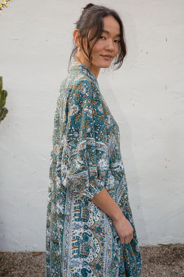 Woman wearing a patterned caftan against a white wall