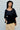 Woman wearing a black top and yellow skirt against a white wall