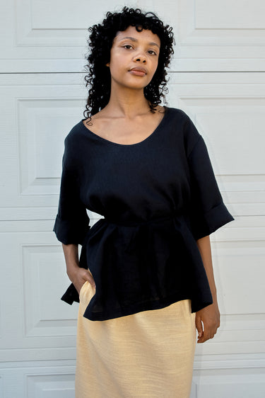Woman wearing a black top and yellow skirt against a white wall