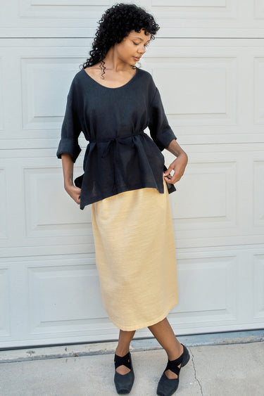 Woman wearing a black top and yellow skirt against a white wall.