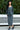 Woman wearing a gray textured outfit standing outdoors with greenery in the background