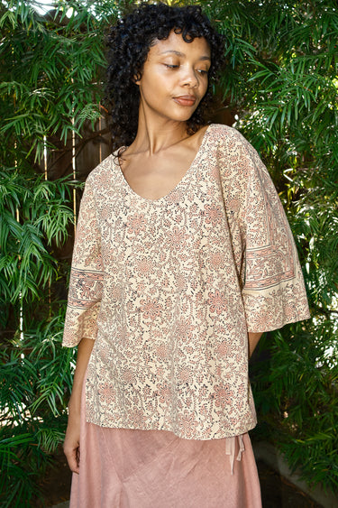 Woman wearing a patterned top and pink skirt against a green leafy background