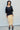 Woman wearing a black top and yellow skirt against a white wall.