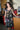 A woman standing in a kitchen wearing a knee-length dress in a black ground tapestry with rainbow suns, moons and stars printed on it.