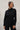 Woman wearing a black long-sleeve jumpsuit with a collar against a white wall