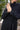 Person wearing a black jumpsuit with hands clasped together outdoors.
