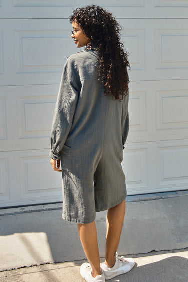 Woman wearing a gray jumpsuit standing in front of a white garage door.