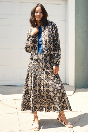 A woman standing in front of a garage door, wearing a midi-length skirt in a geometric tapestry, denim tee top and matching tapestry jacket.
Worn with espadrilles