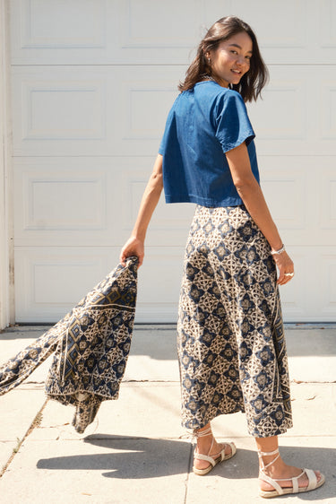 A woman standing in front of a garage door, wearing a midi-length skirt in a geometric tapestry, denim tee top and matching tapestry jacket.
Worn with espadrilles. Back view