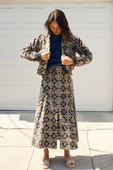 A woman standing in front of a garage door, wearing a midi-length skirt in a geometric tapestry, denim tee top and matching tapestry jacket.
Worn with espadrilles
