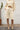 Person wearing an alabaster outfit with shorts and a shirt, standing against a white wall.