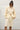 Person wearing an alabaster outfit against a white wall