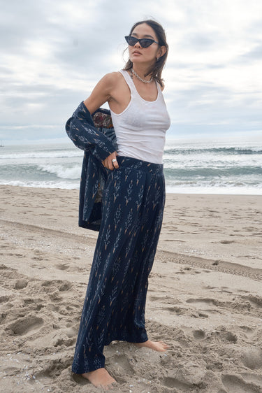 Woman at the beach wearing an ikat low waist trousers, with white tank top and matching jacket.