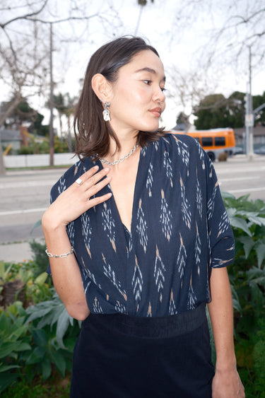 A woman wearing a black Ikat shrug paired with a silver necklace and earrings.