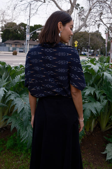 A woman wearing a black Ikat shrug paired with a black corduroy skirt, silver necklace and earrings.