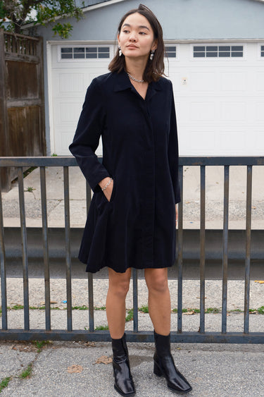 Woman standing outside wearing a black plush corduroy coat dress.