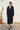 Woman wearing a black outfit standing outdoors with a white wall and plant in the background