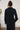 Person wearing a black outfit standing against a textured white wall.