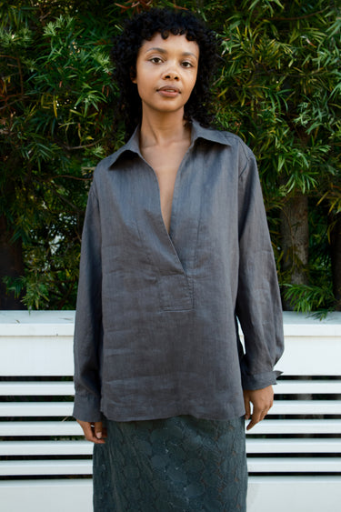Person wearing a dark gray shirt with a deep neckline against a green leafy background.