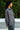 Woman wearing a gray shirt standing outdoors with greenery in the background