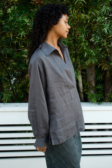 Woman wearing a gray shirt standing outdoors with greenery in the background