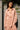 Woman wearing a pink outfit standing against a gray wall with greenery.