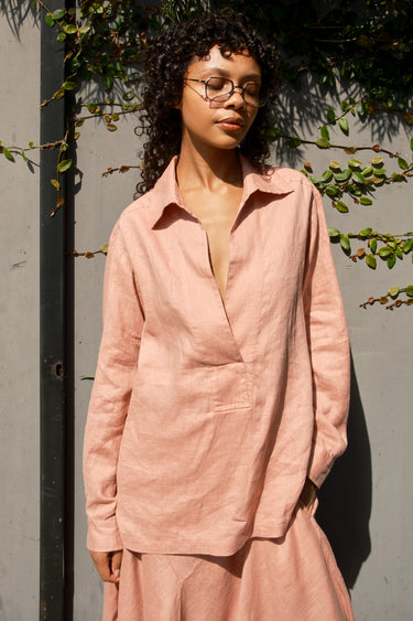 Woman wearing a pink outfit standing against a gray wall with greenery.