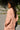 Person wearing a pink outfit standing against a wall with greenery