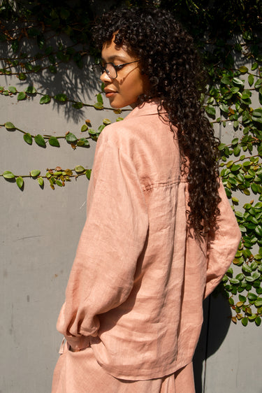 Person wearing a pink outfit standing against a wall with greenery