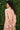Person wearing a pink shirt standing against a green leafy background