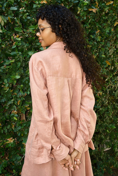 Person wearing a pink shirt standing against a green leafy background