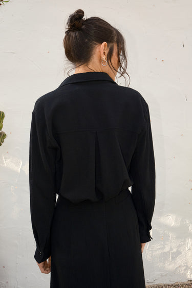 Person wearing a black outfit against a white wall