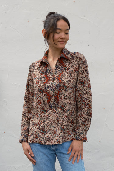 Woman wearing a patterned shirt and blue jeans against a white wall