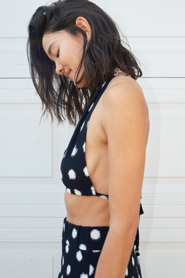 A woman wearing a black and white polka dot bikini top with a V-neckline, posing against a white background. bikini top tied as halter