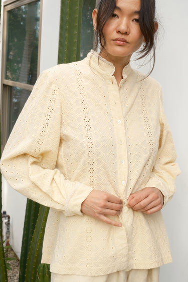 Woman wearing a cream-colored blouse with a textured pattern, standing outdoors.