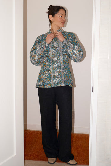 Person wearing a floral blouse and black pants standing in a doorway.