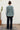 Person wearing a floral blouse and black pants standing against a white wall.