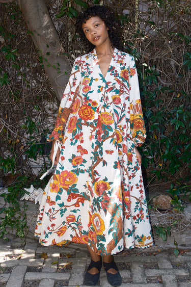 Woman wearing a floral caftan standing outdoors with greenery around
