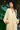 Woman wearing a light yellow dress standing outdoors with green foliage in the background