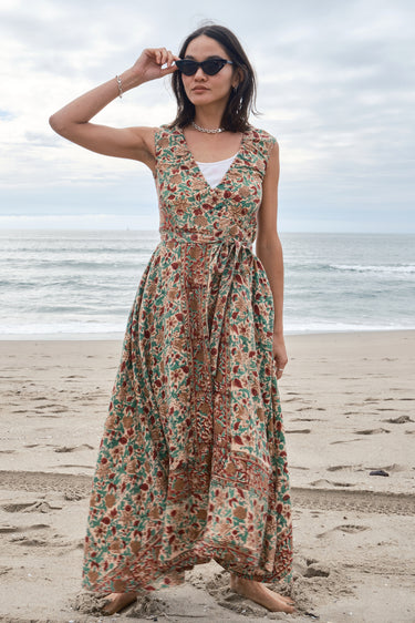 Woman standing on the beach wearing a red, beige and green tapestry maxi wrap dress with a white tank underneath.