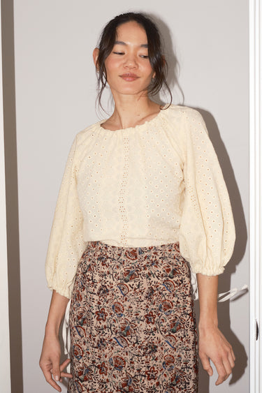 Woman wearing a cream blouse and patterned skirt against a plain background